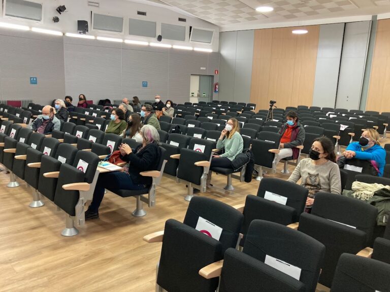 Gent amb mascareta asseguda, separada entre si, en les butaques d'una sala d'actes.