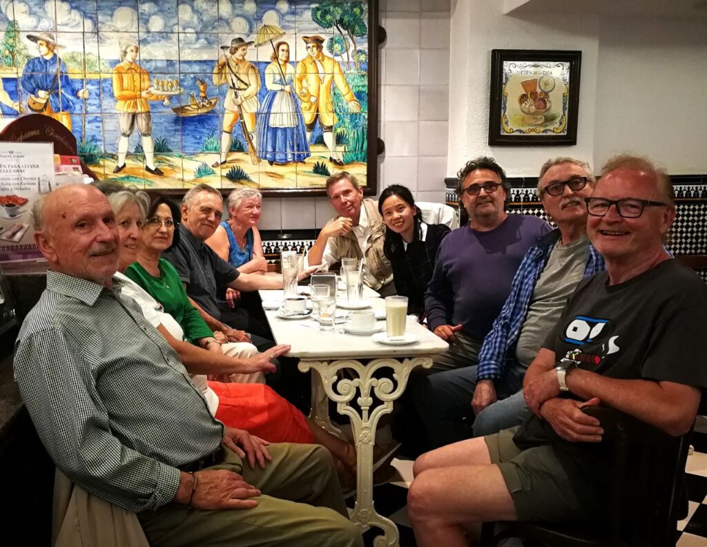 Deu esperantistes al voltant d'una taula de marbre a l'horchateria Santa Catalina de València, amb gots d'orxata; al fons, un plafó de ceràmica valenciana i el terra de quadres blancs i negres.