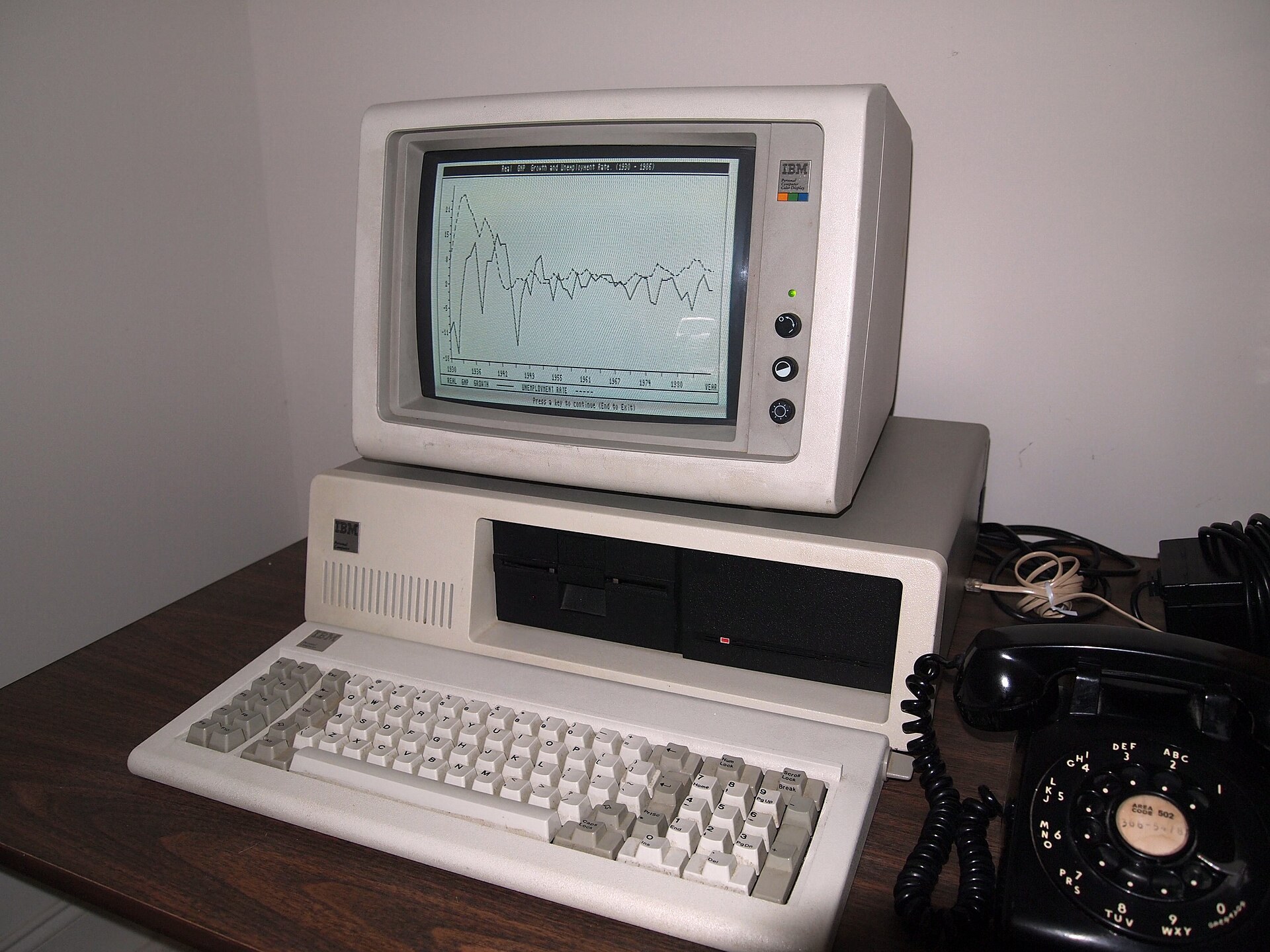 Bejĝa IBM PC kun sia ekrano, du disketiloj kaj la klavaro antaŭe, sur tablo.