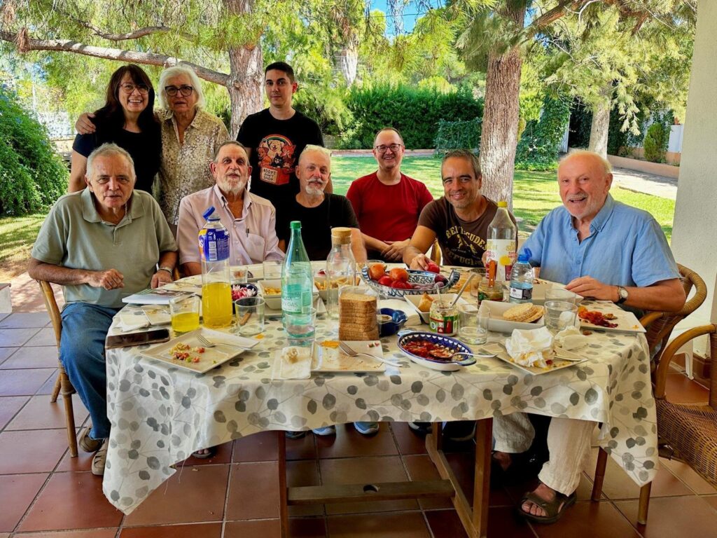 Nou persones del grup dinant al voltant d'una taula, en un jardí.