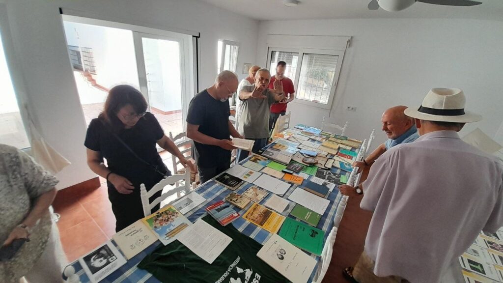 L'exposició de llibres en esperanto: una taula llarga plena de llibres i revistes, amb diverses persones mirant-los.