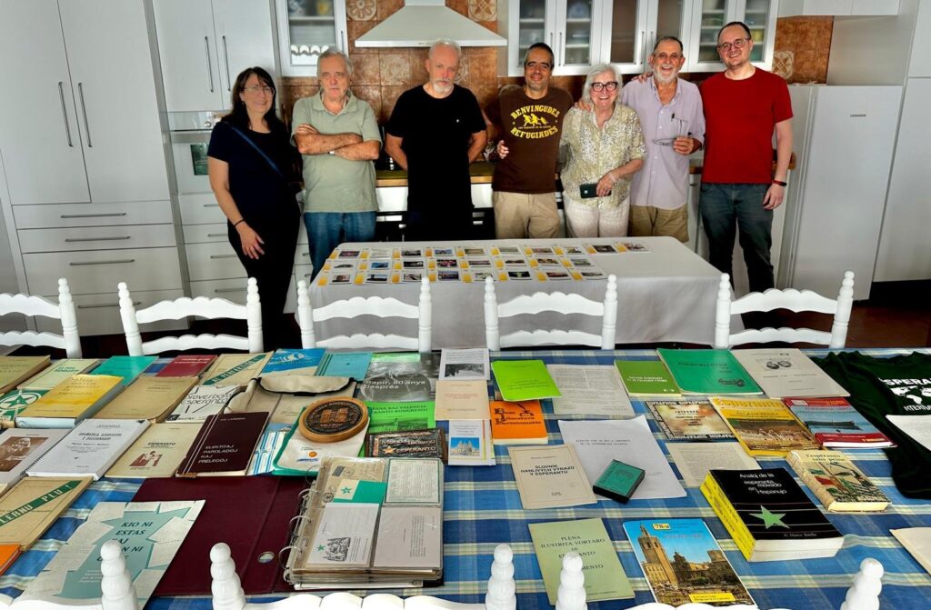 Set persones del grup dretes darrere d'una taula coberta de llibres, revistes i fullets en esperanto.
