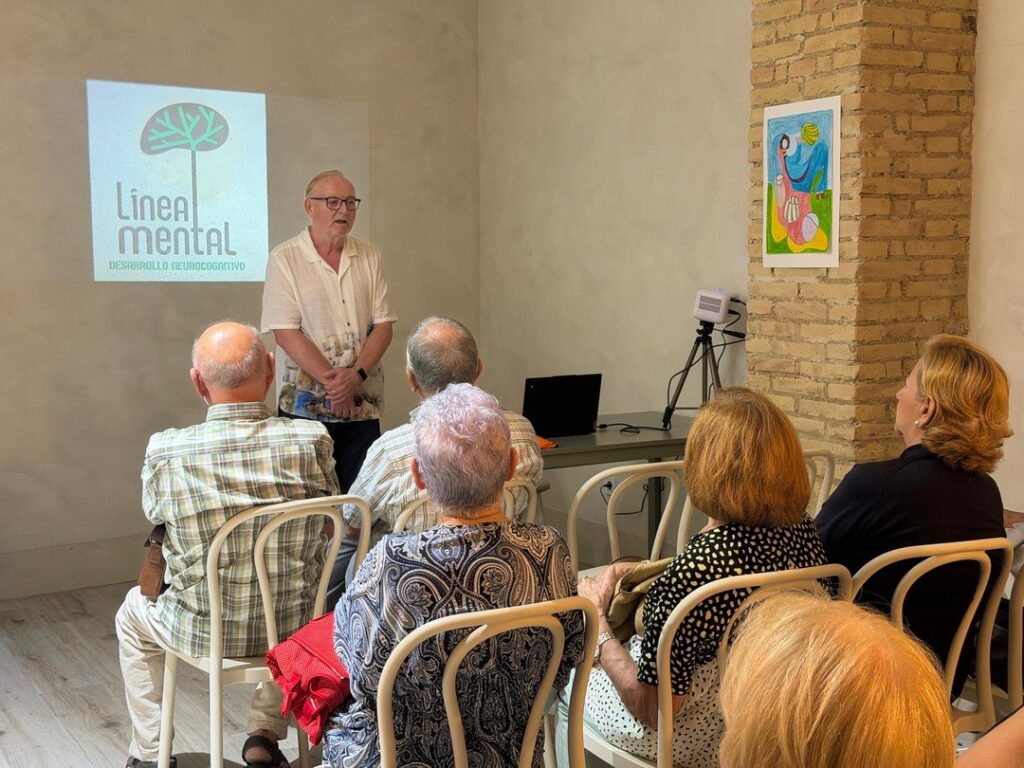 Eduardo, dret davant del logotip de Línea Mental projectat a la paret, parla al públic assegut en cadires blanques.