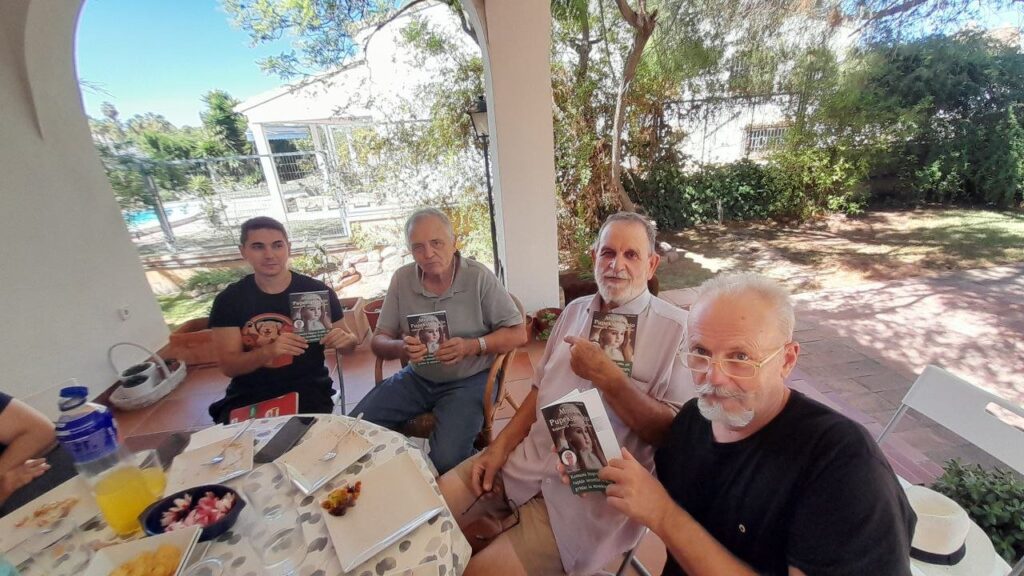 Quatre persones del grup assegudes a taula, cadascuna amb un exemplar del llibre «Monda Pupekspozicio».